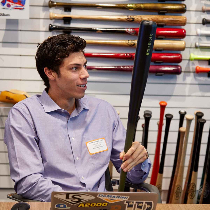 A man sits at a table holding a Louisville Slugger MLB Prime Signature Series CY22 Christian Yelich Game Model Wood Baseball Bat (WBL2435010).