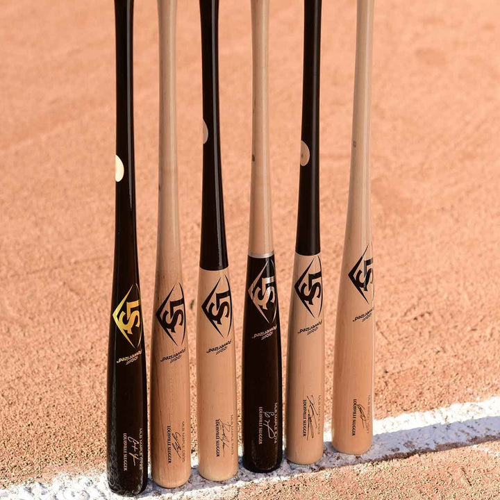 Five Louisville Slugger MLB Prime Signature Series CY22 Christian Yelich Game Model wood bats (WBL2435010) stand vertically together on the field, leaning on the dirt near a white chalk baseline.