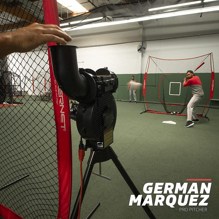 A baseball pitcher practices batting in an indoor facility using the PowerNet Launch F-Lite Portable Pitching Machine (model 1194), set up on a tripod and operated by a coach. The PowerNet brand is featured at the bottom right.