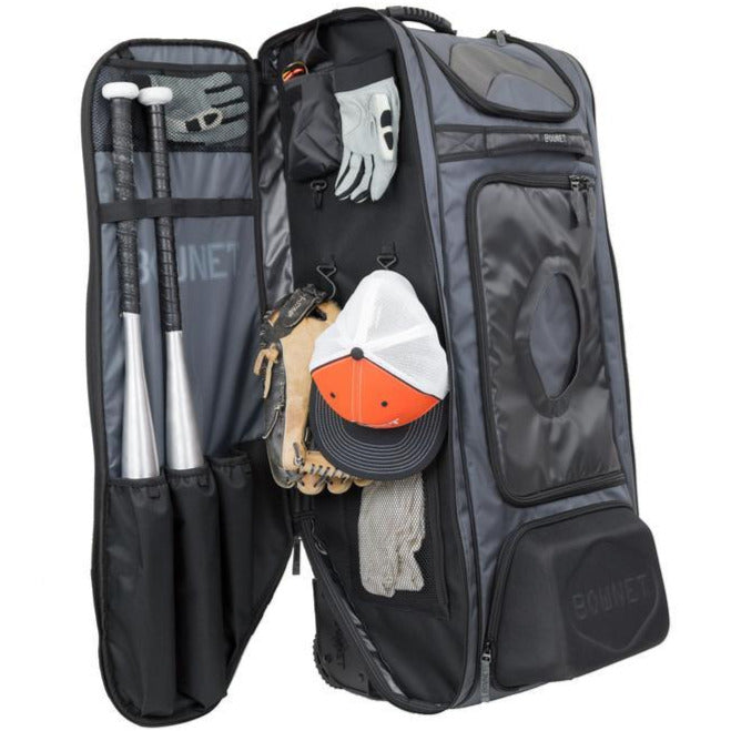 The Bownet Commander Wheeled Catcher's Bag (BN-COMMANDER BAG) by Bownet stands open, showing baseball bats, gloves, a hat, batting gloves, and cleats neatly organized in separate compartments.