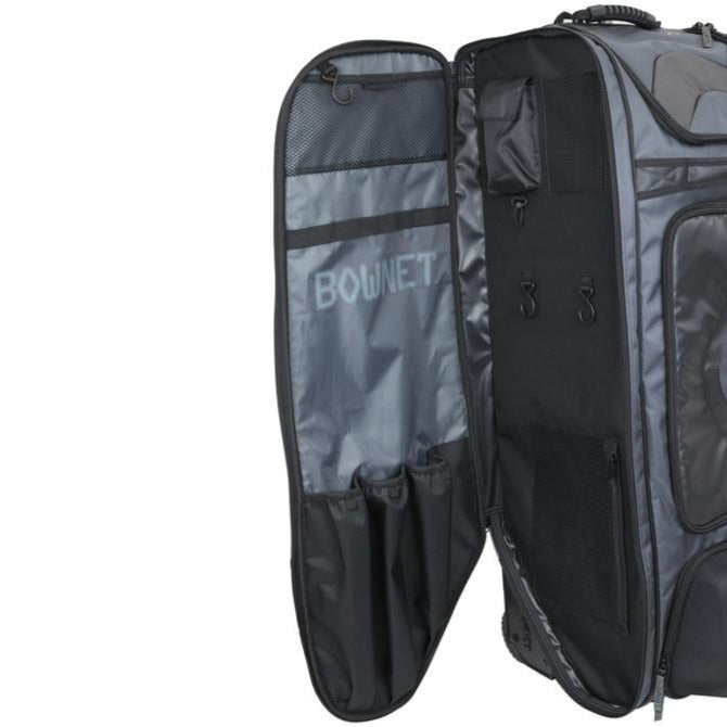 The Bownet Commander Wheeled Catcher's Bag (BN-COMMANDER BAG) in black and gray is shown open, revealing interior pockets and mesh compartments. The Bownet logo appears inside the flap, making it ideal for baseball gear.