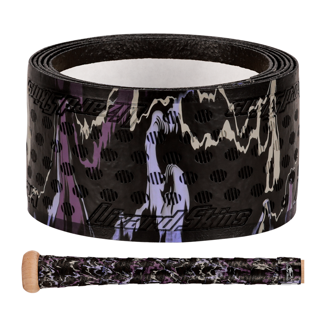 The Lizard Skins DSP Ultra Camo 1.1mm Bat Grip, in black with purple, white, and tan camo plus black polka dots, is shown rolled up and wrapped on a wooden bat handle.