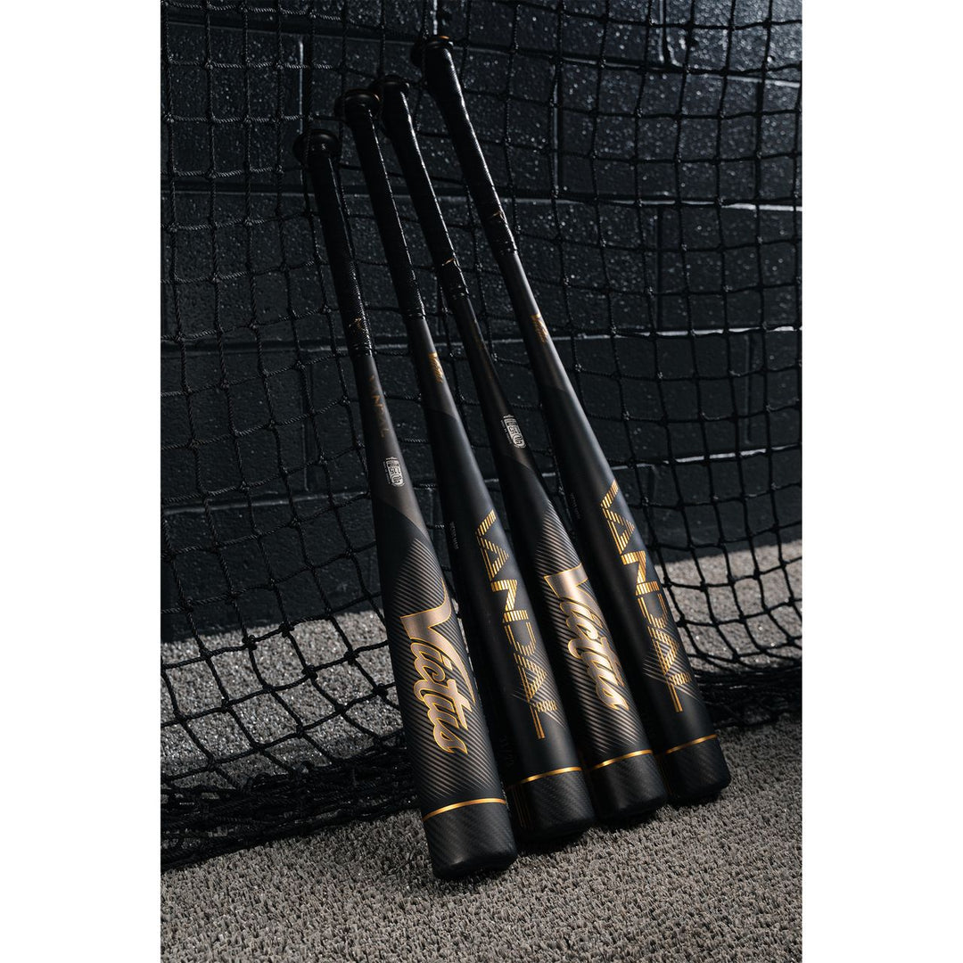 Four black and gold Victus Vandal 2 (-8) USSSA baseball bats stand upright against a netted wall on gray carpet, showcasing their sleek, modern design—ideal for serious players seeking top performance.
