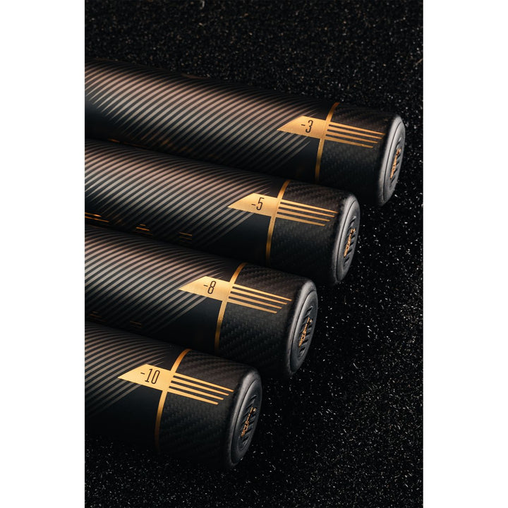 Four black cylindrical objects with gold accents and numbers (-3, -5, -8, -10) are arranged in a row on a textured black surface, featuring a sleek carbon fiber design like the 2022 Victus Vandal 2 (-8) USSSA Baseball Bat by Victus.