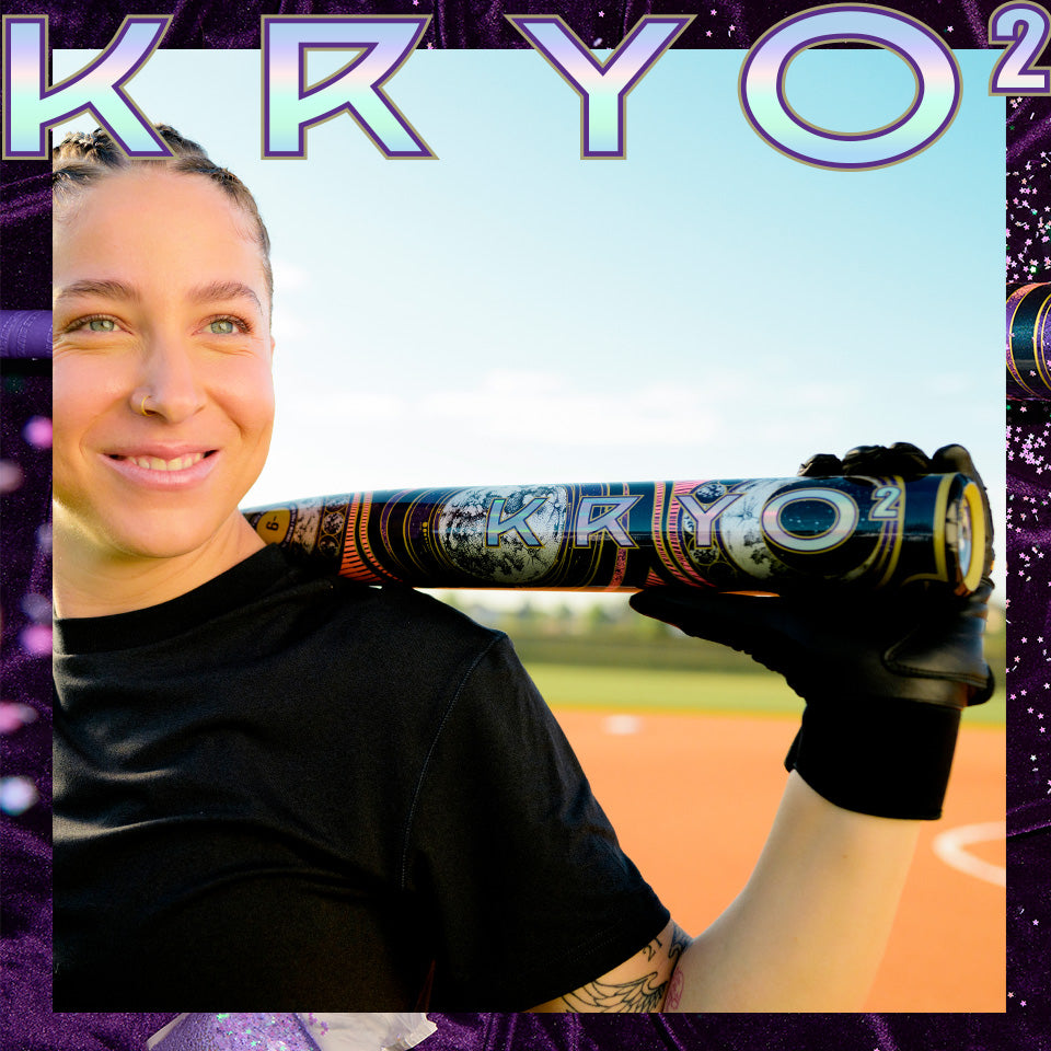 A person in a black shirt holds the 2027 Louisville Slugger Kryo2 Empress Fastpitch Softball Bat over their shoulder on a baseball field, smiling at the camera.