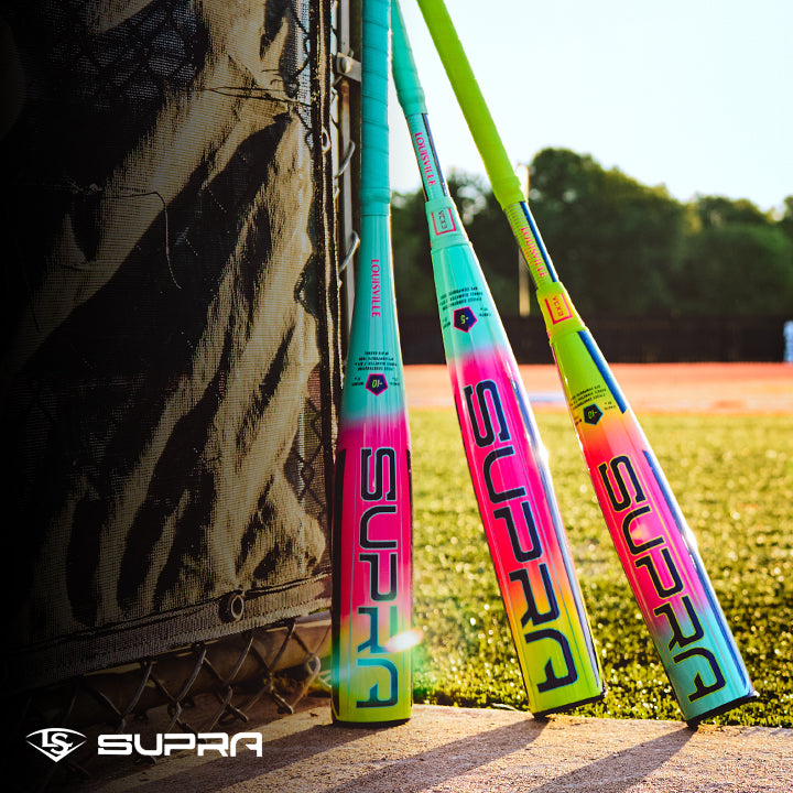 Three vibrant Louisville Slugger 2027 Supra JBB (-10) USSSA bats with gradient designs lean against a black net on a sunny field, lush grass and trees behind them. The Louisville Slugger logo appears in the lower left corner.