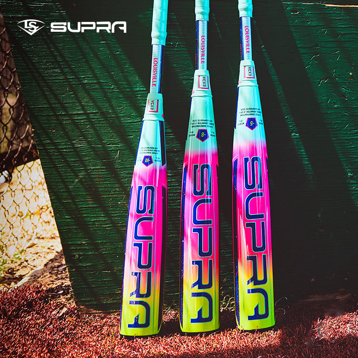 Three vibrant 2027 Louisville Slugger Supra (-5) 2 3/4" USSSA Baseball Bats (WBL4253010) in teal, pink, and yellow gradient rest against a green fence. Louisville Slugger branding and APX Composite Technology are clearly visible.