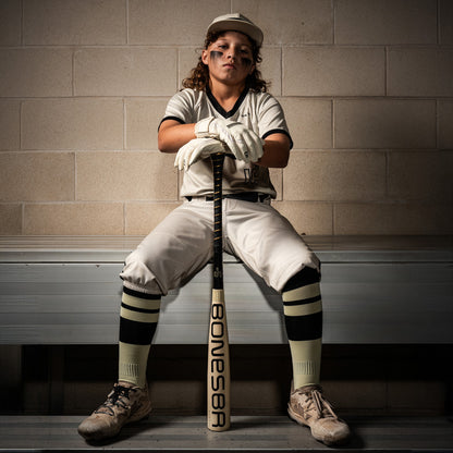 A girl sits on a bench holding a Warstic 2026 Bonesaber Hybrid (-10) USA Baseball Bat (MBBSH25UBWH10), her grip confident as she gazes out at the field.