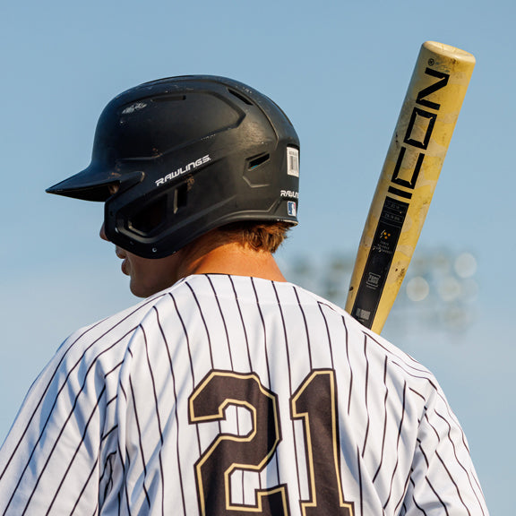 A baseball player wearing a black helmet and a white pinstripe jersey with the number 21 stands with a yellow bat resting on his shoulder, facing away from the camera.