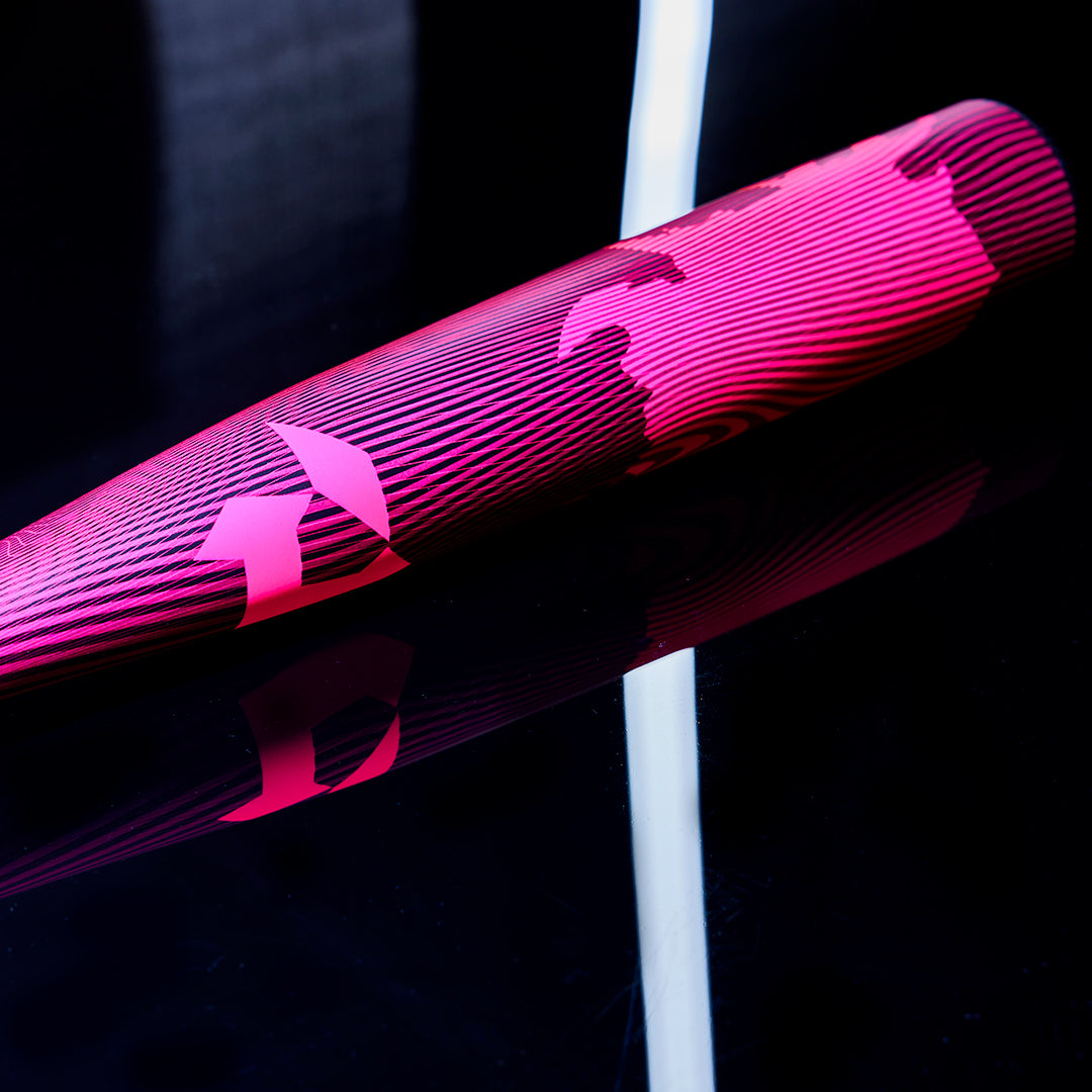 A close-up of the 2024 DeMarini Voodoo One Neon Pink (-3) BBCOR Baseball Bat (WBD2557010) lies on a glossy black surface, its bold pink and black design reflecting light.