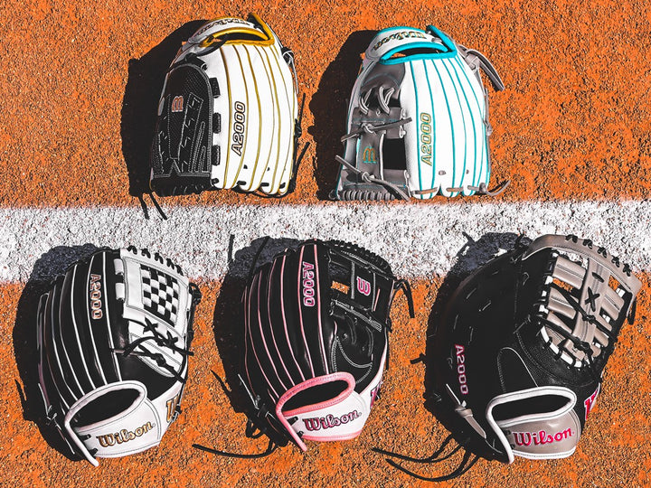 Five baseball gloves with different designs and colors are laid out on an orange field, three above a white line and two below it. The gloves display various patterns and the brand Wilson and A2000.