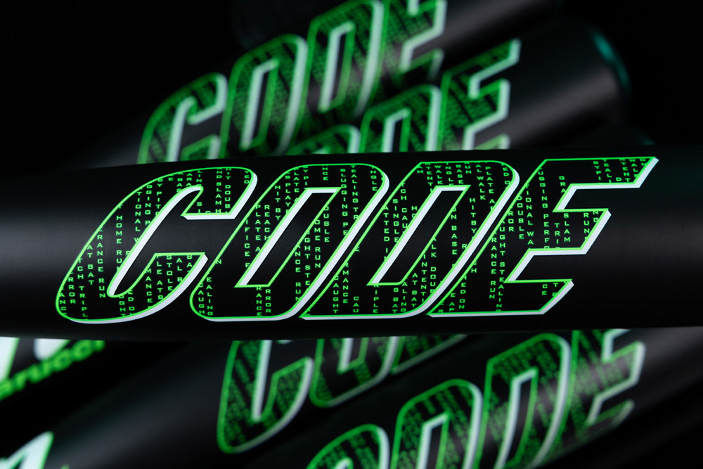 The word CODE appears in bold, futuristic letters filled with green matrix-style binary, set on a dark background with overlapping layers—styled like the high-performance Marucci 2025 Code (-5) USSSA Baseball Bat MSBCD5.