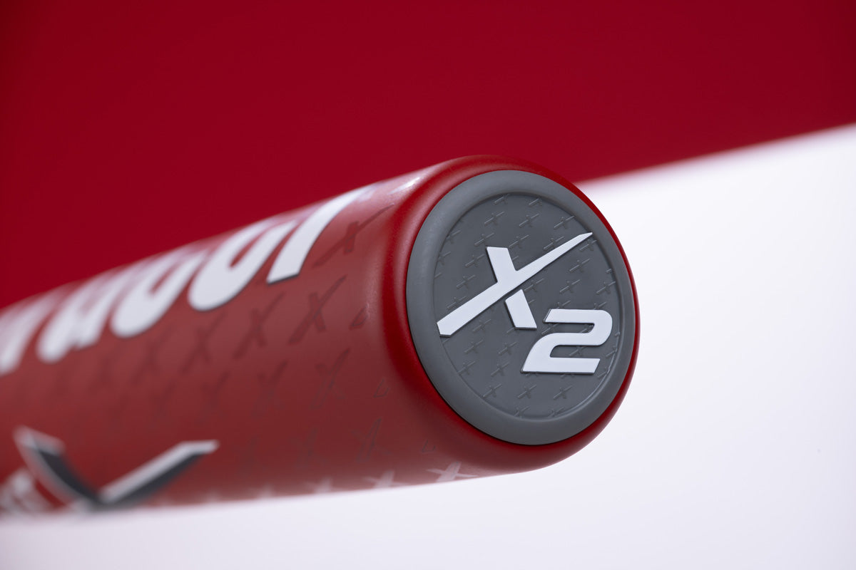 Close-up of the end cap on the Marucci CATX2 (-11) USA Baseball Bat (MSBCX211USA), showcasing the bold X2 in white on gray. The red bat features a textured surface, Anti-Vibration Technology, and part of the Marucci logo is visible.