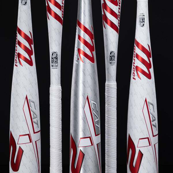 Four Marucci CAT X baseball bats, white with red accents, stand upright against a black background. The bats have wrapped handles and display the CAT X logo and certification labels.