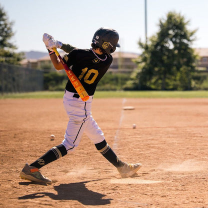 A young baseball player in a black #10 jersey swings the 2025 Easton Hype Fire JBB (-10) 2 3/4" USSSA Baseball Bat (EJB5HYP10) by Easton on a sunny field, dust rising as trees and fences frame the action.