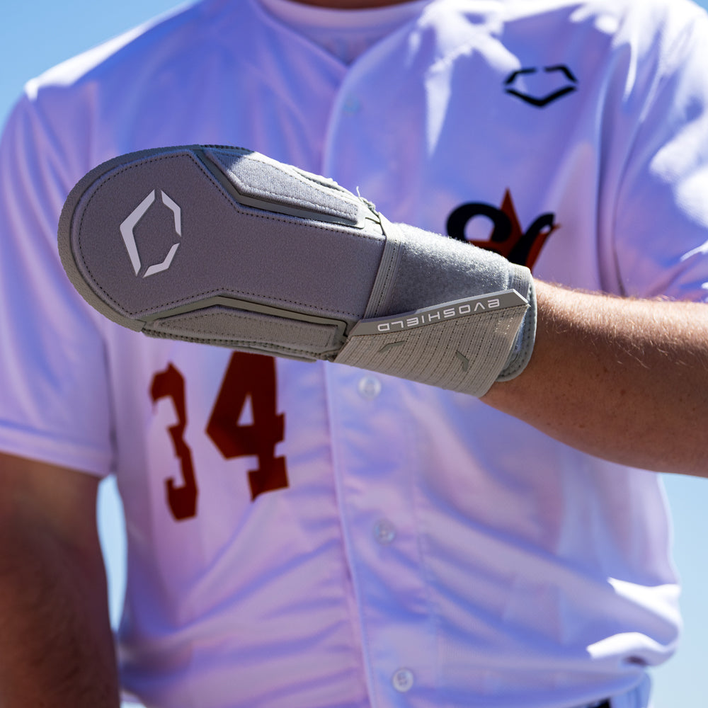 A baseball player in a white jersey with number 34 wears the EvoShield Sliding Mitt 2.0 (WB57537) by EvoShield on their left hand for added protection.