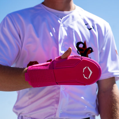 A baseball player in a white jersey gives a thumbs up, proudly showing off an EvoShield Sliding Mitt 2.0: WB57537 by EvoShield on their left hand for extra protection.