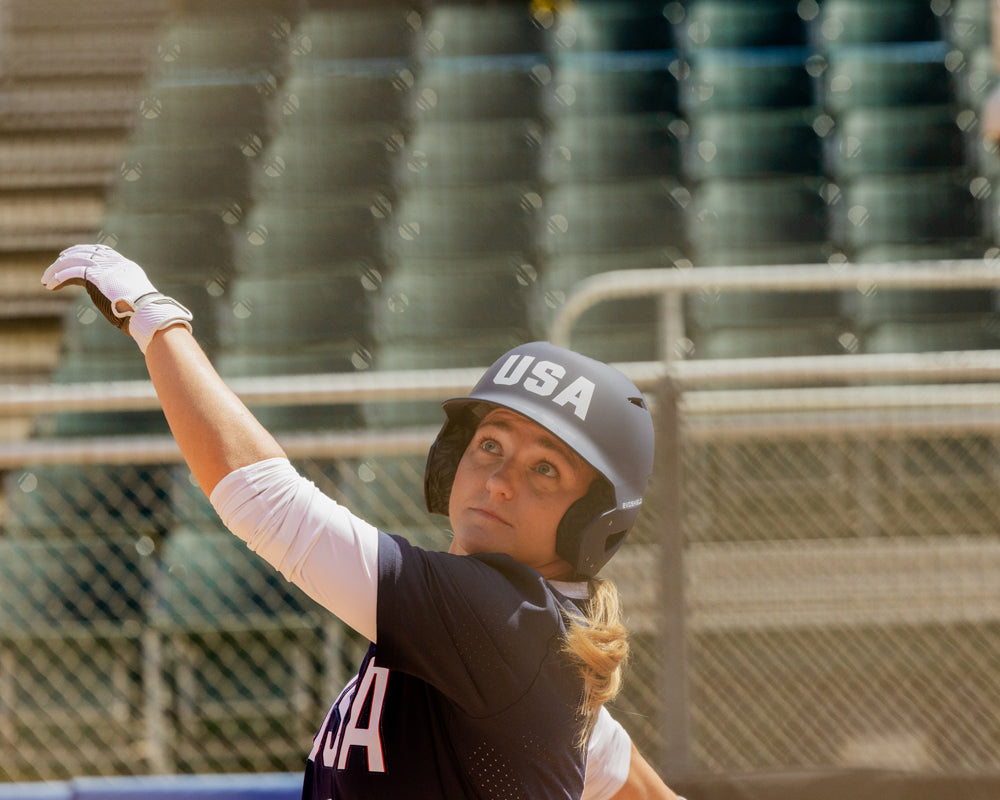 A woman wearing a helmet holds the 2025 Easton Ghost Unlimited (-9) Fastpitch Softball Bat (EFP5GHUL9) by Easton.