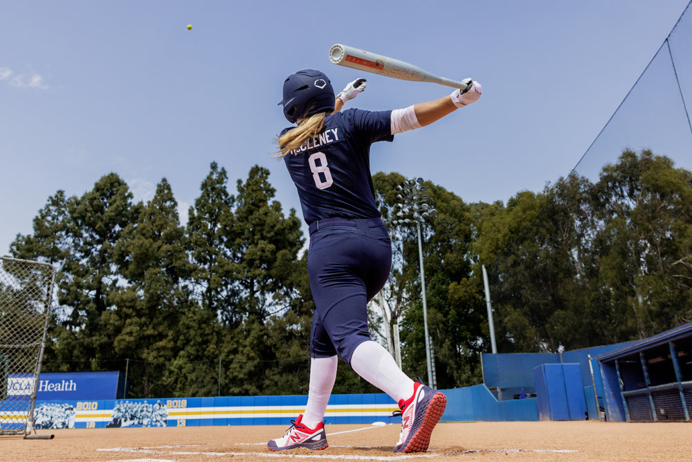 A softball player in a navy uniform with the number 8 swings the 2025 Easton Ghost Unlimited (-9) Fastpitch Softball Bat (EFP5GHUL9) on an outdoor field, with trees and blue stadium seats visible in the background.