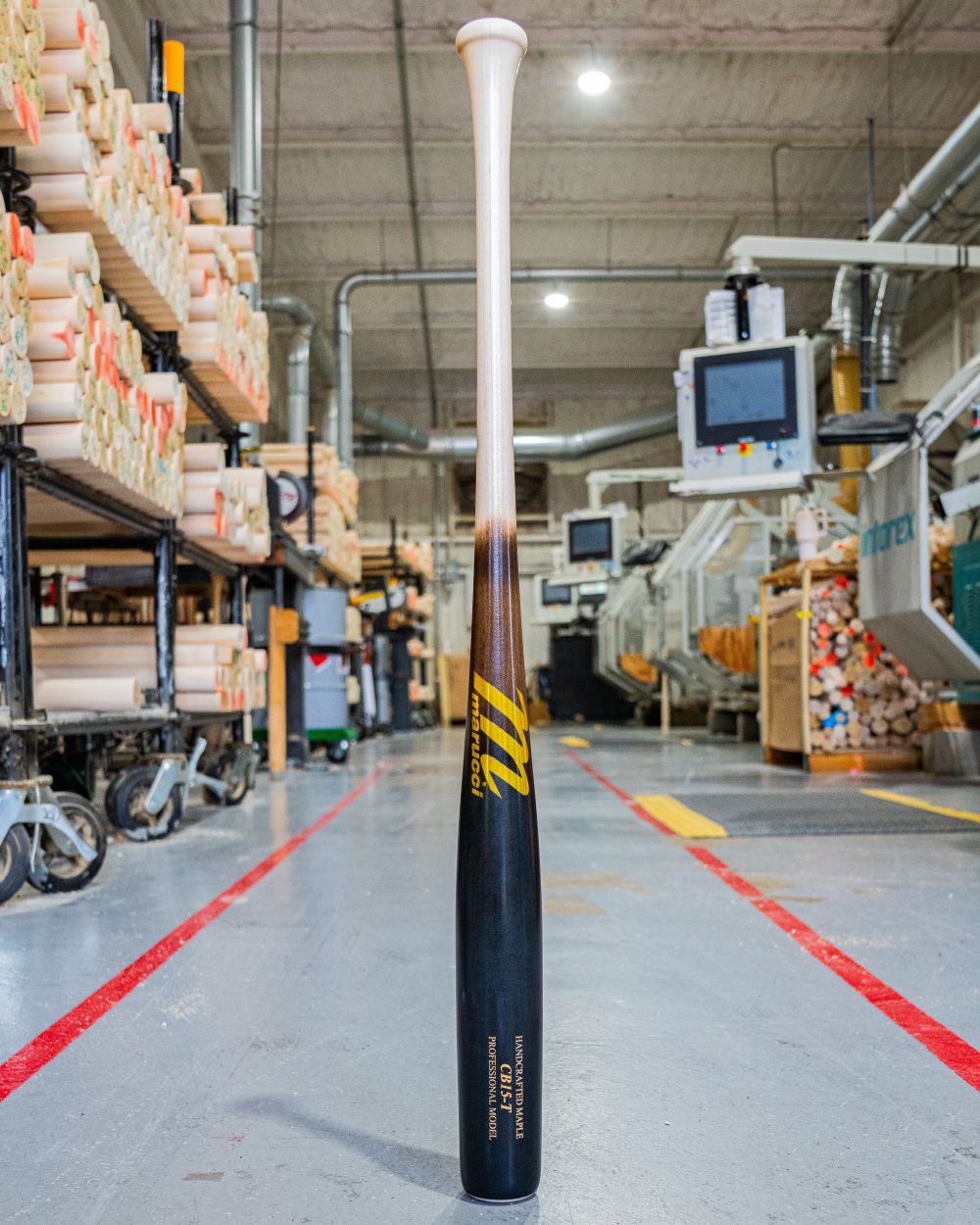 A Marucci CB15 Torpedo Pro Model Maple Wood Bat: MVE5CB15T stands upright on the factory floor, its black and natural finish reflecting expert craftsmanship, designed for performance by Marucci.