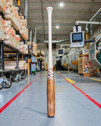 A Marucci AP5 Torpedo Pro Model Maple Wood Bat: MVE5AP5T stands upright on the factory floor, surrounded by machinery and stacks of wood—ideal for power hitters who demand quality from Marucci. Bright lights shine on polished concrete floors.