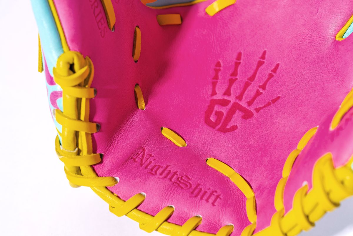 A close-up of the Marucci NightShift Robert Sponge 11.75" glove features bright pink inner leather, yellow laces, turquoise accents, and a handprint with "GC" plus "NightShift" embossed on premium Japanese-tanned steerhide.