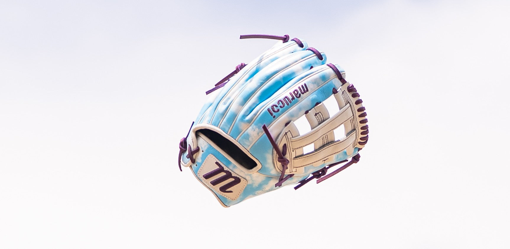 A light blue and white baseball glove with purple laces is floating in the air against a cloudy sky background.