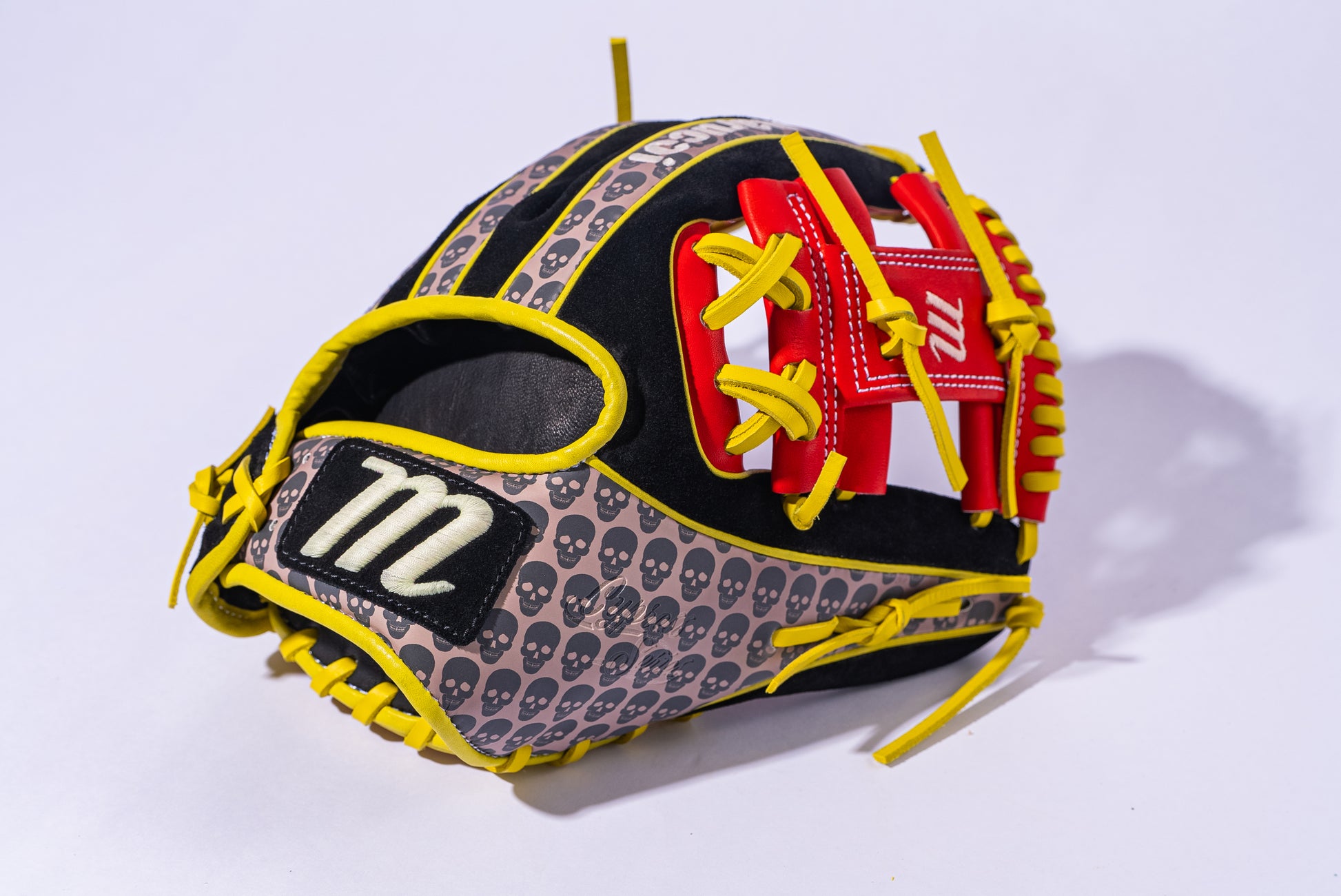 The Marucci NightShift Hot Head 11.5" Baseball Glove (MFGNTSHFT-0406) features black Japanese-tanned steerhide, yellow laces, red accents, small gray skulls, and a white "m" logo on a black patch. Displayed on a white background.