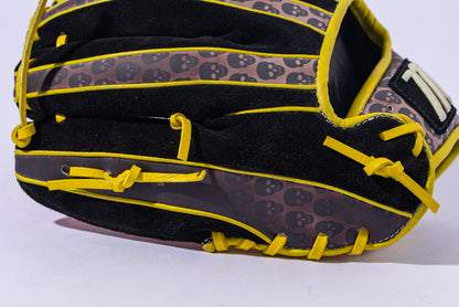 A Marucci NightShift Hot Head 11.5" Baseball Glove (MFGNTSHFT-0406) made from Japanese-tanned steerhide, with yellow laces and small skulls on brown leather, rests on a white surface.