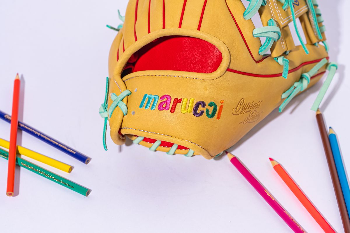 The Marucci NightShift Coloring Book 11.5" Baseball Glove (MFGNTSHFT-0404) features colorful "marucci" stitching and light blue laces on Japanese-tanned steerhide, shown with colored pencils scattered on a white background.