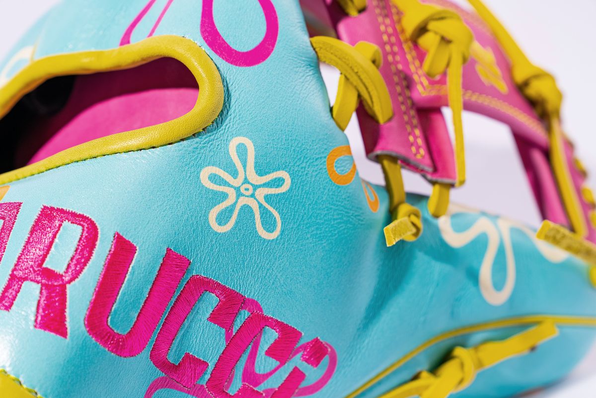 A close-up of the Marucci NightShift Robert Sponge 11.75" Baseball Glove (MFGNTSHFT-0407), crafted from Japanese-tanned steerhide, with blue leather, pink, yellow, and white accents, abstract shapes, and bold embroidered lettering by Marucci.