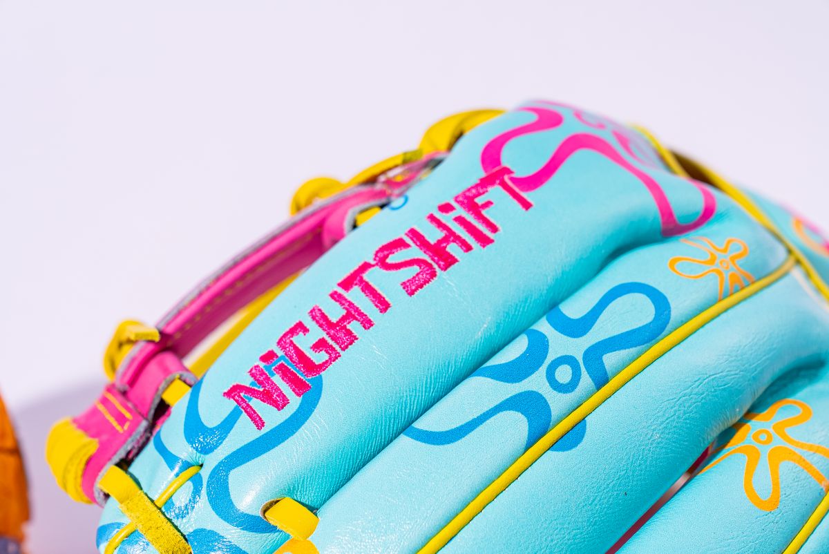 A close-up of the Marucci NightShift Robert Sponge 11.75" Baseball Glove (MFGNTSHFT-0407) shows Japanese-tanned steerhide in turquoise with pink, yellow, and blue patterns and bold pink “NIGHTSHIFT” embroidery.