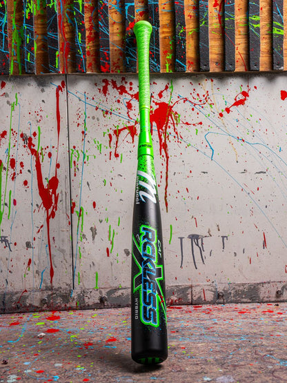 The Marucci CAT X RCKLESS Hybrid (-3) BBCOR Baseball Bat (MCBCRH DEMO) stands upright, its neon green handle and black barrel with bold Reckless graphics showcasing Marucci’s striking design against a paint-splattered wall.