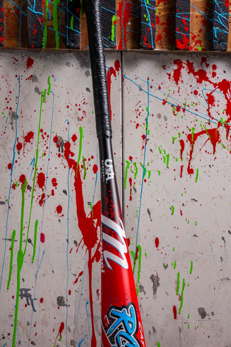 A Marucci 2026 CAT X RCKLESS (-8) 2 5/8" USA Baseball Bat (MSBCR8USA) rests against a wall splattered with red, green, and blue paint.