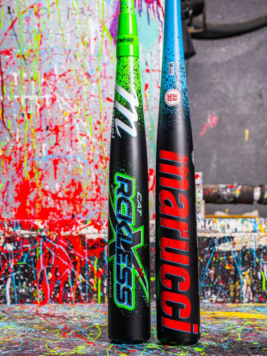 Two baseball bats stand upright against a paint-splattered background. The left is a black Marucci 2026 CAT X RCKLESS Hybrid (-3) BBCOR Baseball Bat with green accents; the right is black with red and blue details and Marucci branding.