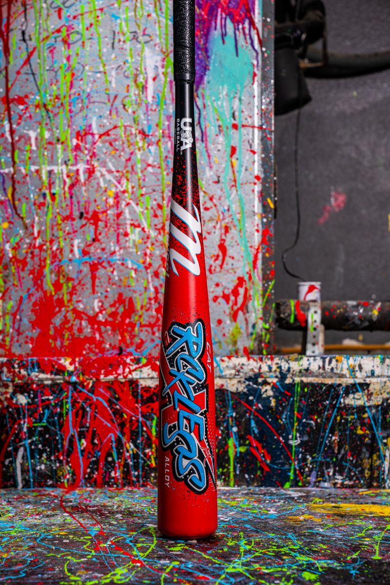 The 2026 Marucci CAT X RCKLESS (-8) USA Baseball Bat stands upright with bold RCKLESS lettering, set against a vibrant paint-splattered backdrop for an energetic and artistic look.