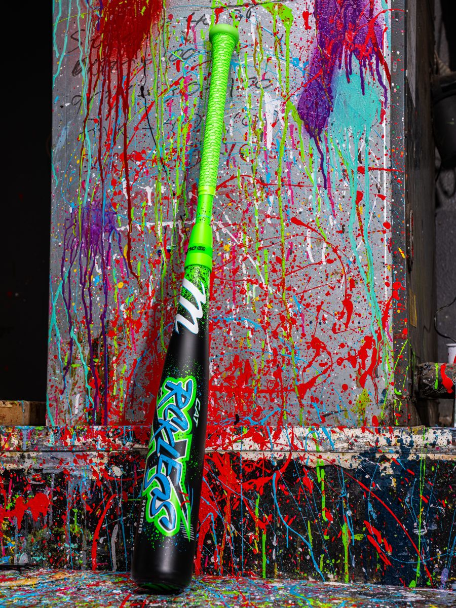 A Marucci 2026 CAT X RCKLESS Hybrid (-10) 2 3/4" USSSA Baseball Bat (MSBCRH10 DEMO) with black, green, and colorful paint splatters stands out against a concrete wall.