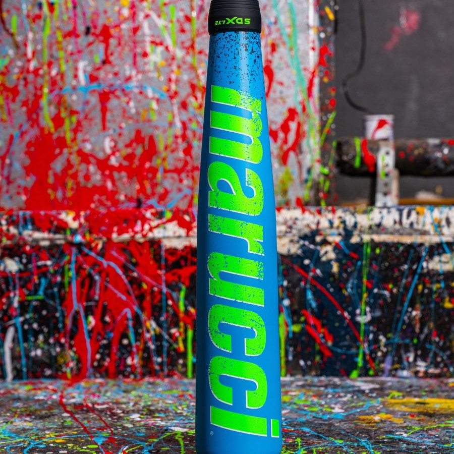 A blue Marucci baseball bat with green lettering stands upright in front of a background splattered with vibrant red, yellow, blue, and green paint.