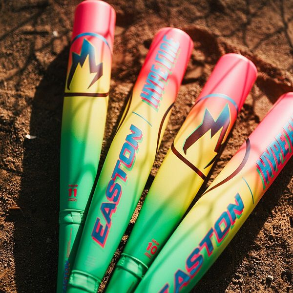 Three vibrant baseball bats, including the 2026 Easton Hype Fire (-11) USA Baseball Bat (EUS6HYP11) by Easton with a green, yellow, and pink gradient design, rest on sandy ground in sunlight.