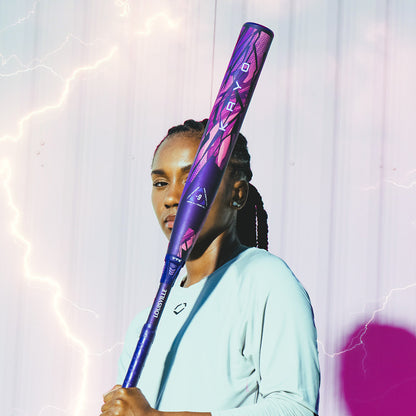 A person with braided hair stands against a light wall holding the Louisville Slugger 2026 Kryo Thundernight Fastpitch Softball Bat upright by their shoulder, with lightning effects visible in the background.