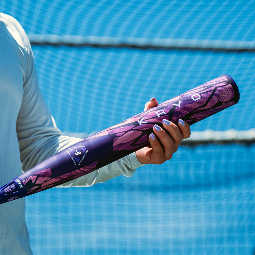 Person holding a purple and black kryo fastpitch bat with a blurred blue background