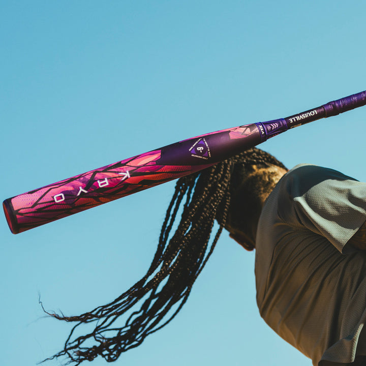 Person swinging a pink and purple kryo fastpitch softball bat against a clear blue sky