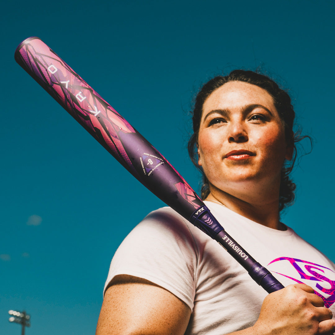 Woman holding a purple and pink kryo fastpitch softball bat against a clear blue sky