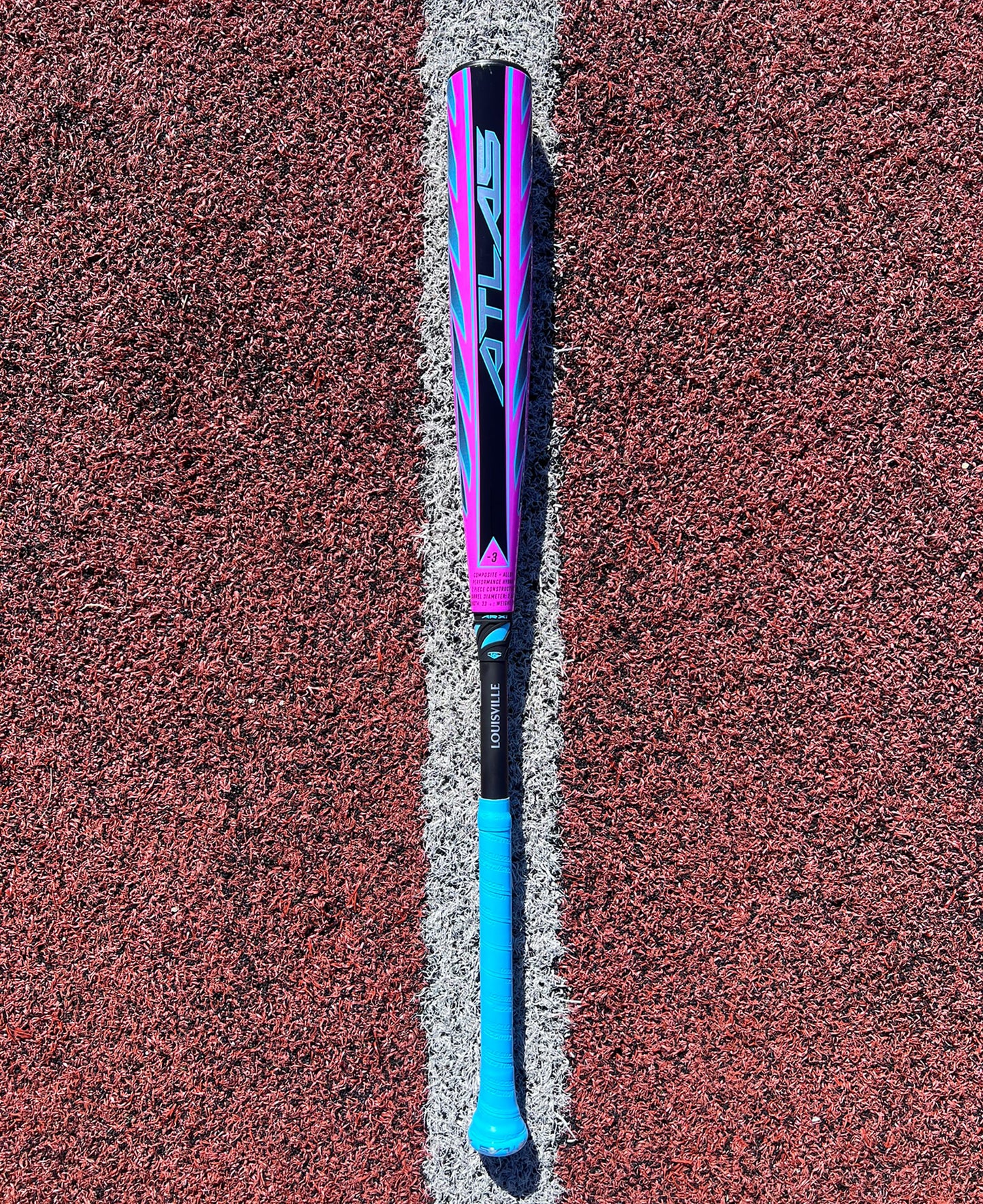 The 2026 Louisville Slugger Atlas Hybrid (-3) BBCOR Baseball Bat (WBL4114010) featuring a blue and pink design is centered on a red textured field, perfectly aligned with a white line beneath it.
