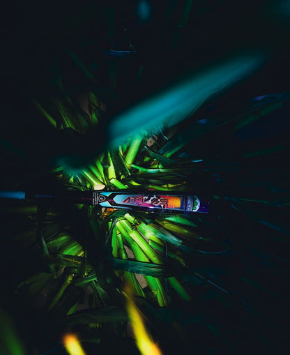 The 2026 Louisville Slugger Atlas A51 (-3) BBCOR Baseball Bat (WBL4180010), featuring a vibrant geometric design, rests among lush green leaves under dramatic, moody lighting.