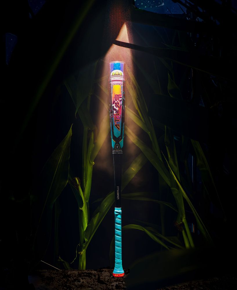 The 2026 Louisville Slugger Atlas A51 (-3) BBCOR Baseball Bat (WBL4180010) stands upright, bathed in light with blue and red accents, surrounded by tall green corn stalks at night.