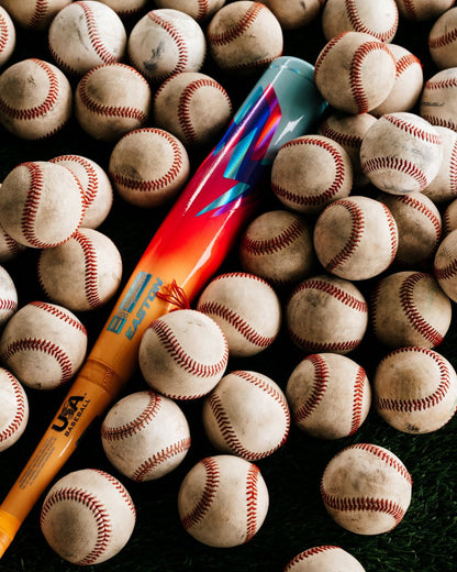 A vibrant 2027 Easton Hype Fire (-11) 2 5/8″ USA Baseball Bat (EUS7HYP11) by Easton rests on the grass, encircled by several white baseballs with red stitching.