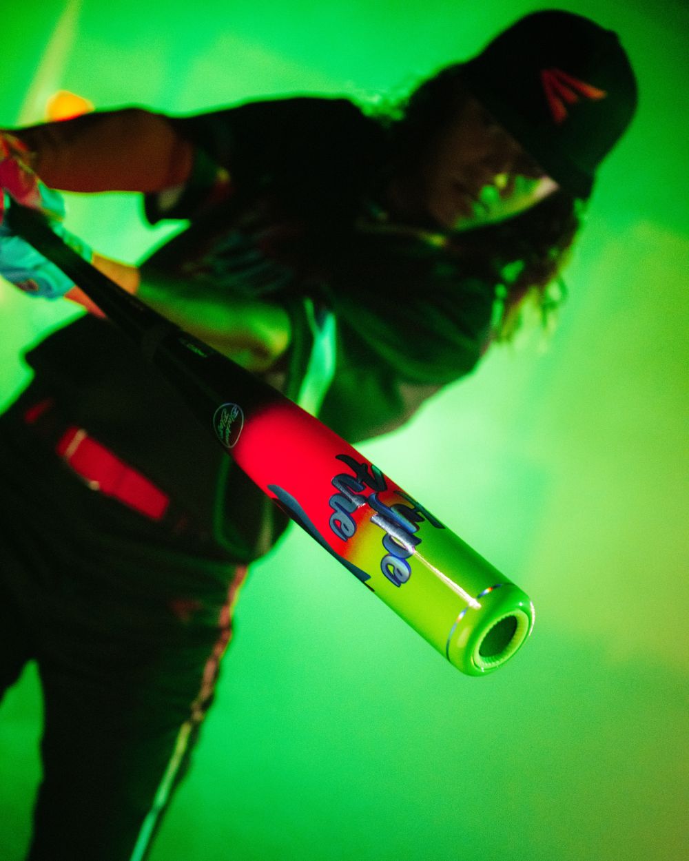 A baseball player in a dark uniform holds the 2027 Easton Hype Fire (-10) 2 3/4″ USSSA Baseball Bat (EUT7HYP10) by Easton toward the camera, as green lighting and mist in the background create a dramatic and intense atmosphere.