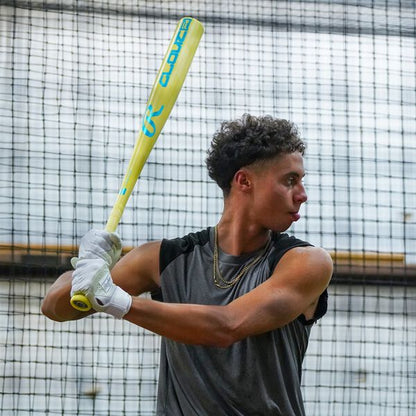 A young man in a sleeveless shirt and gloves grips a yellow 2026 Rawlings Clout AI (-3) BBCOR Baseball Bat (RBB6C3), getting ready to swing in an indoor batting cage with a netted background.