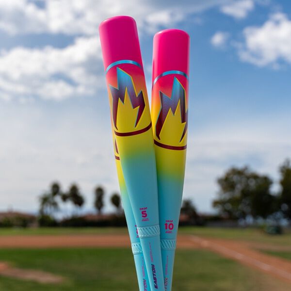 Two vibrant Easton Hype Fire (-5) 2 3/4" USSSA Baseball Bats (EUT6HYP5) stand upright, featuring bold flame designs, with a baseball field and partly cloudy sky blurred in the background.